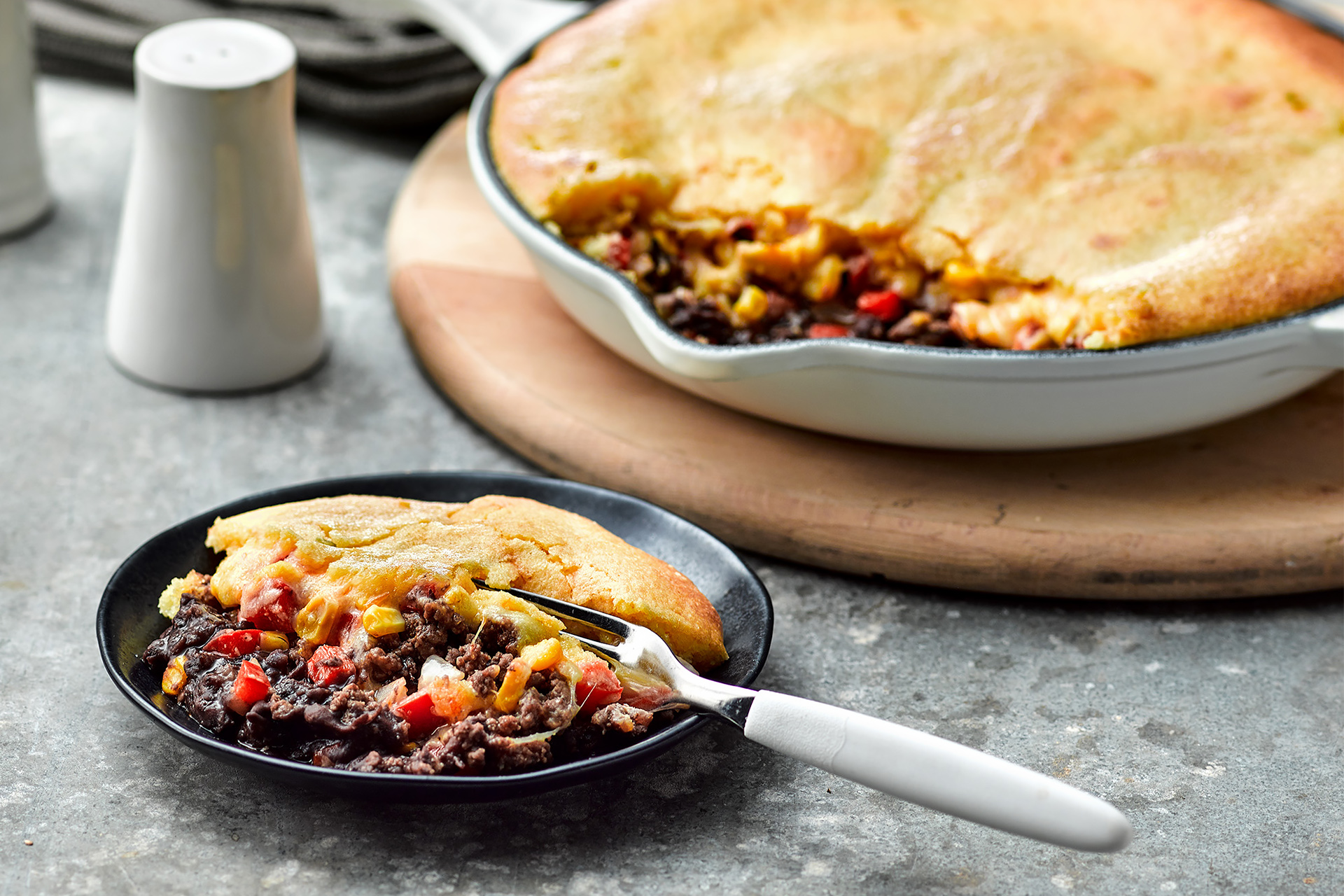 Black bean and cornbread tamale pie resting on a black plate with a fork
